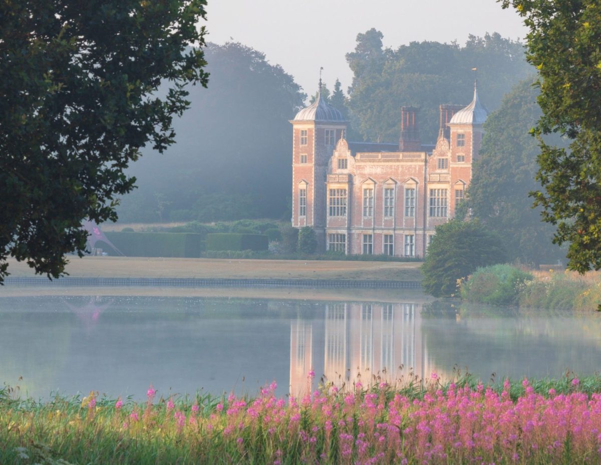 Blickling Hall in the early morning with the lake glistening in front of the grand house.