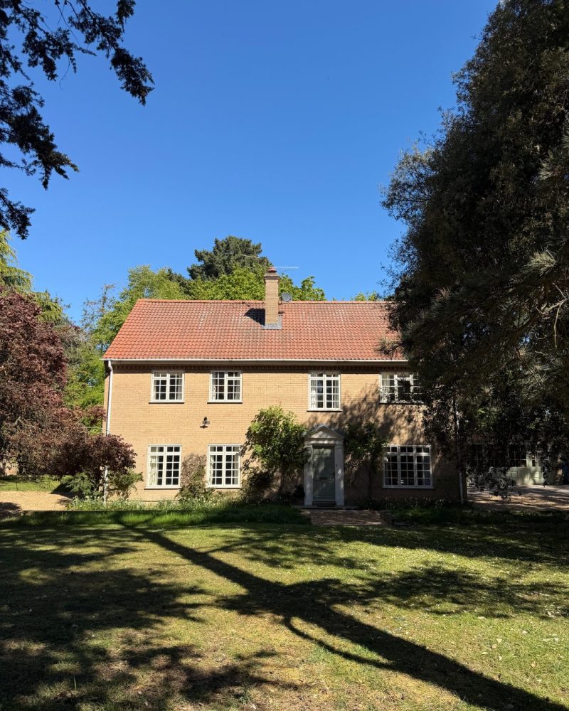 A large pale brick house with a pale blue front door and bright blue skies overhead.