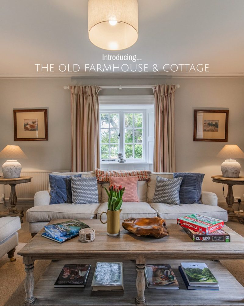 A large oak coffee table displays a selection of books, magazines and house games in a large living room with pale soft seating.