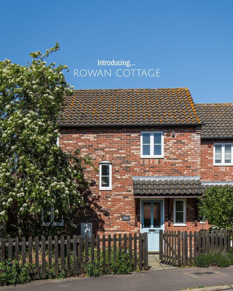 A brick cottage with a pale blue front door and brown picket fence out front.
